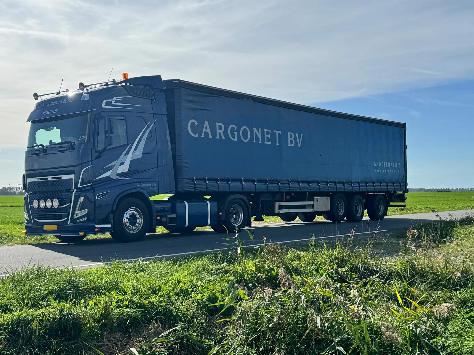 Blauwe tautliner met Cargonet op de oplegger, van opzij gefotografeerd op een landelijke weg.